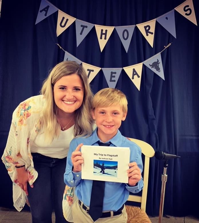 A teacher is smiling with a student who is holding up his book from project Author's Tea