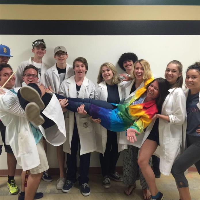  Miranda Thornton is wearing a colorful lab coat and lifted up by her students