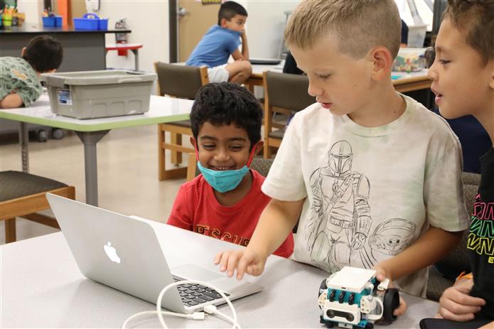  Image of 3 students smiling at a computer with a LEGO robot they've programmed