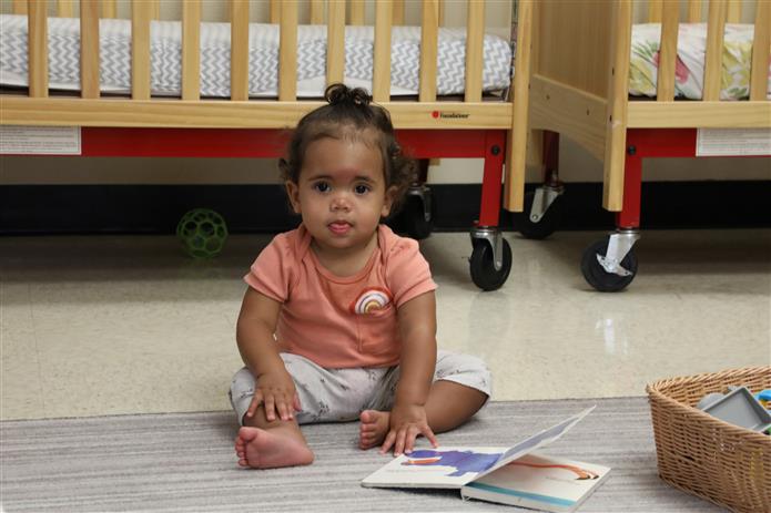  Image of infant sitting up next to an open book