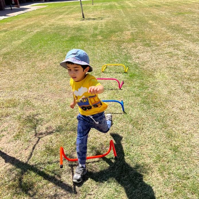 little boy jumps over a hurdle while wearing a bucket hat